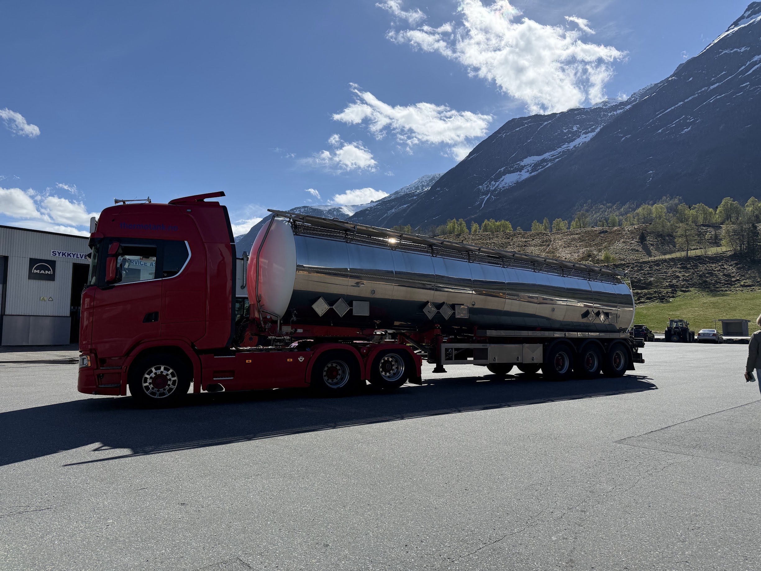 Rød tankbil med natur og snøkledde fjell i bakgrunnen.
