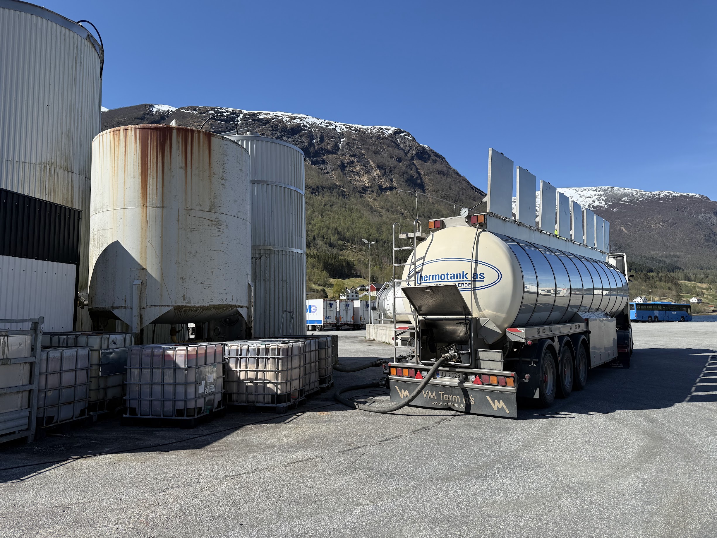 En tankbil som tanker og gjøres klar for transport, med vakker natur og snøkledde fjelltopper i bakgrunnen.