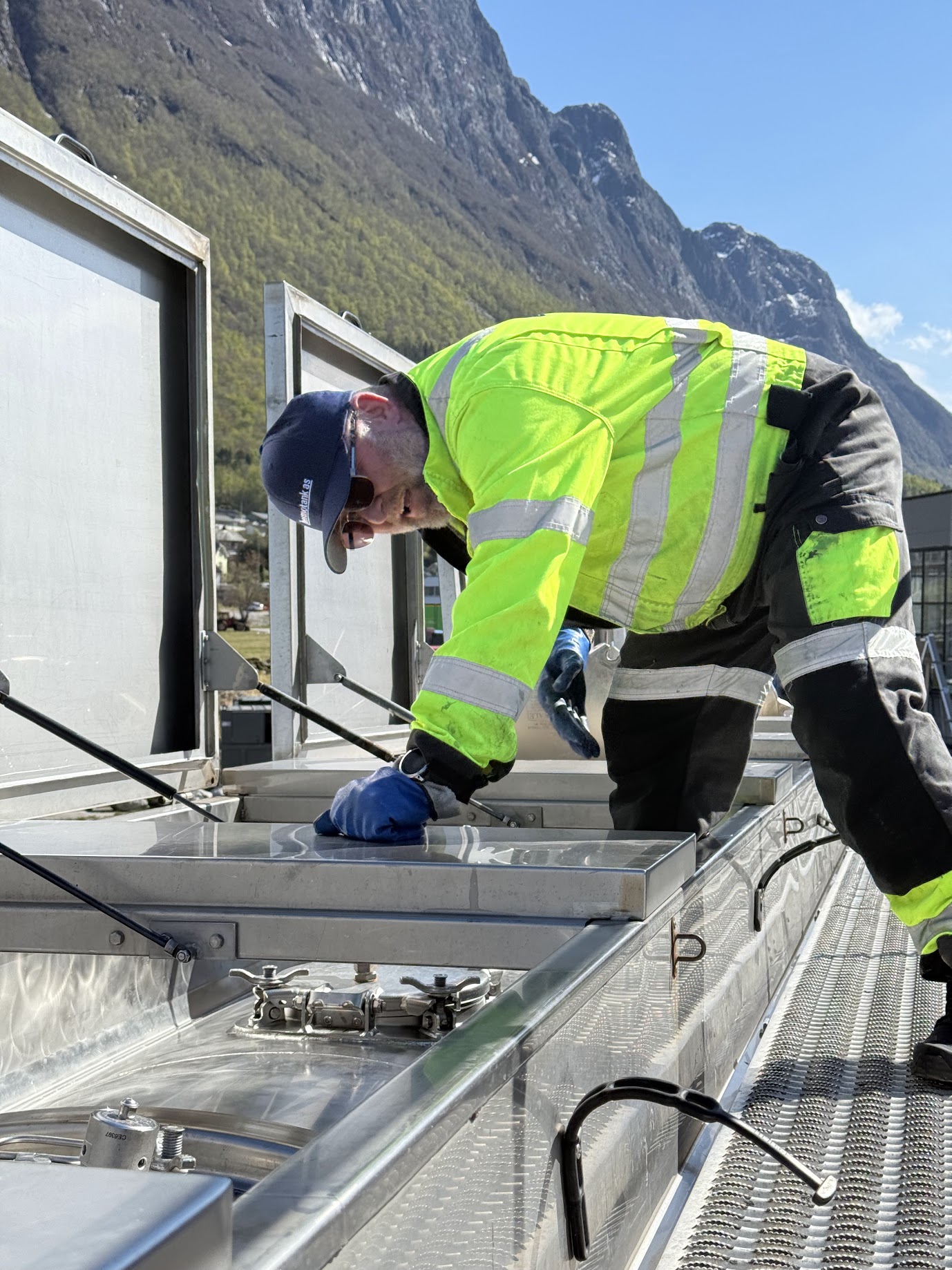 Ansatt i Thermotank AS gjør klar tankbil til transport. Natur og bratte fjell i bakgrunnen kan sees.