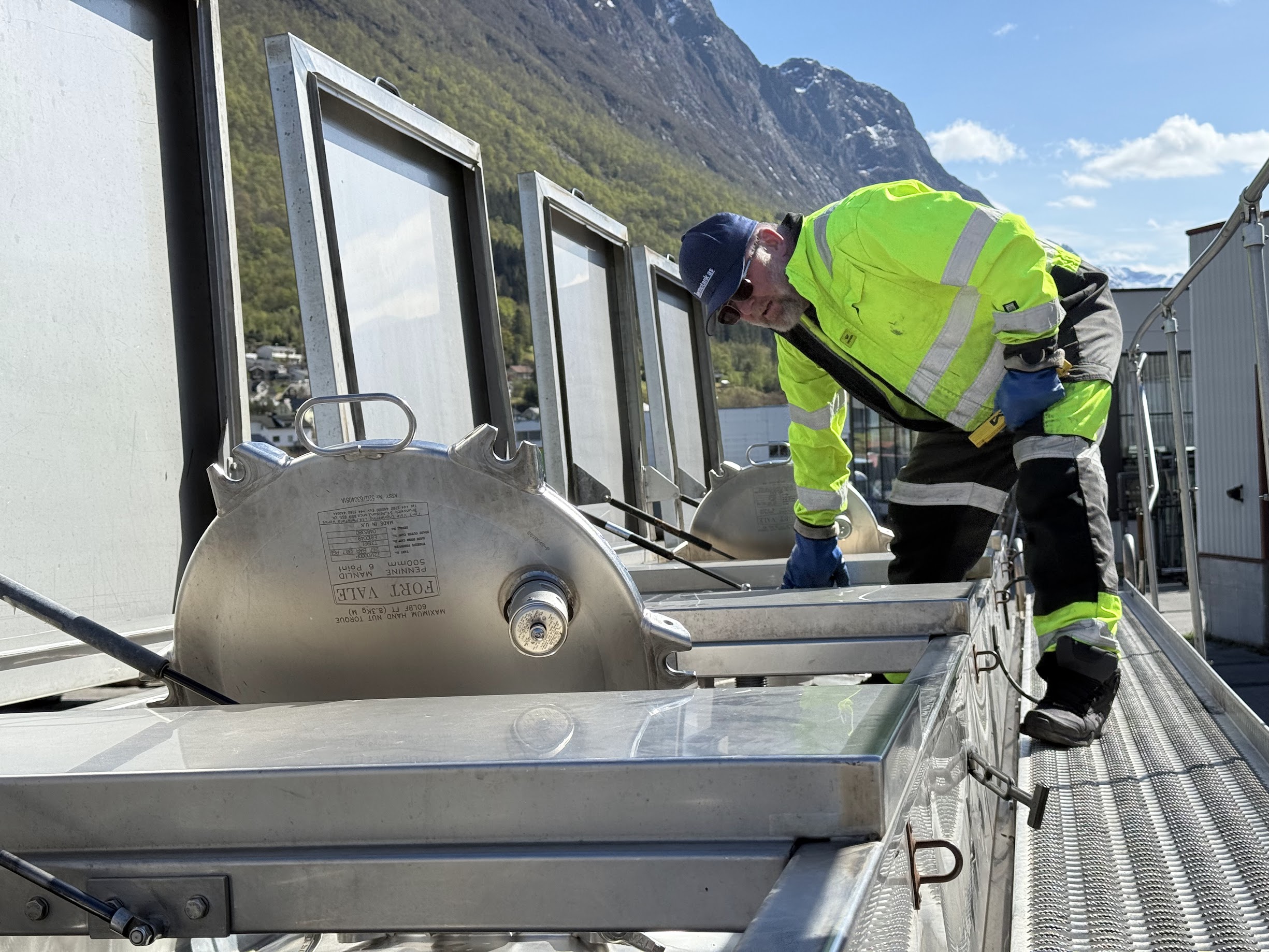 Ansatt i Thermotank AS gjør klar tankbil til transport. Natur og bratte fjell i bakgrunnen kan sees.